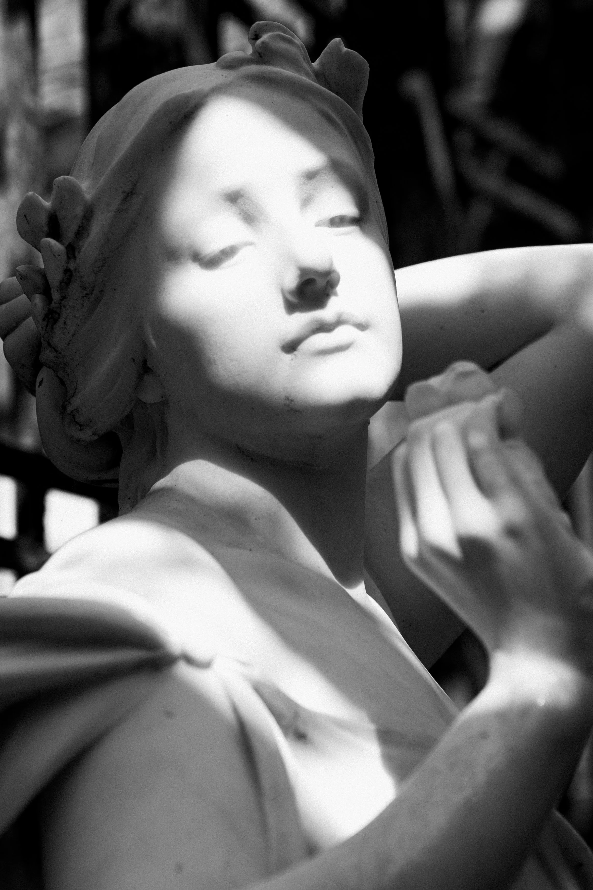 Black and white photograph of a classical-style sculpture of a woman with a serene expression, floral crown, and closed eyes, resting her chin on her hand.