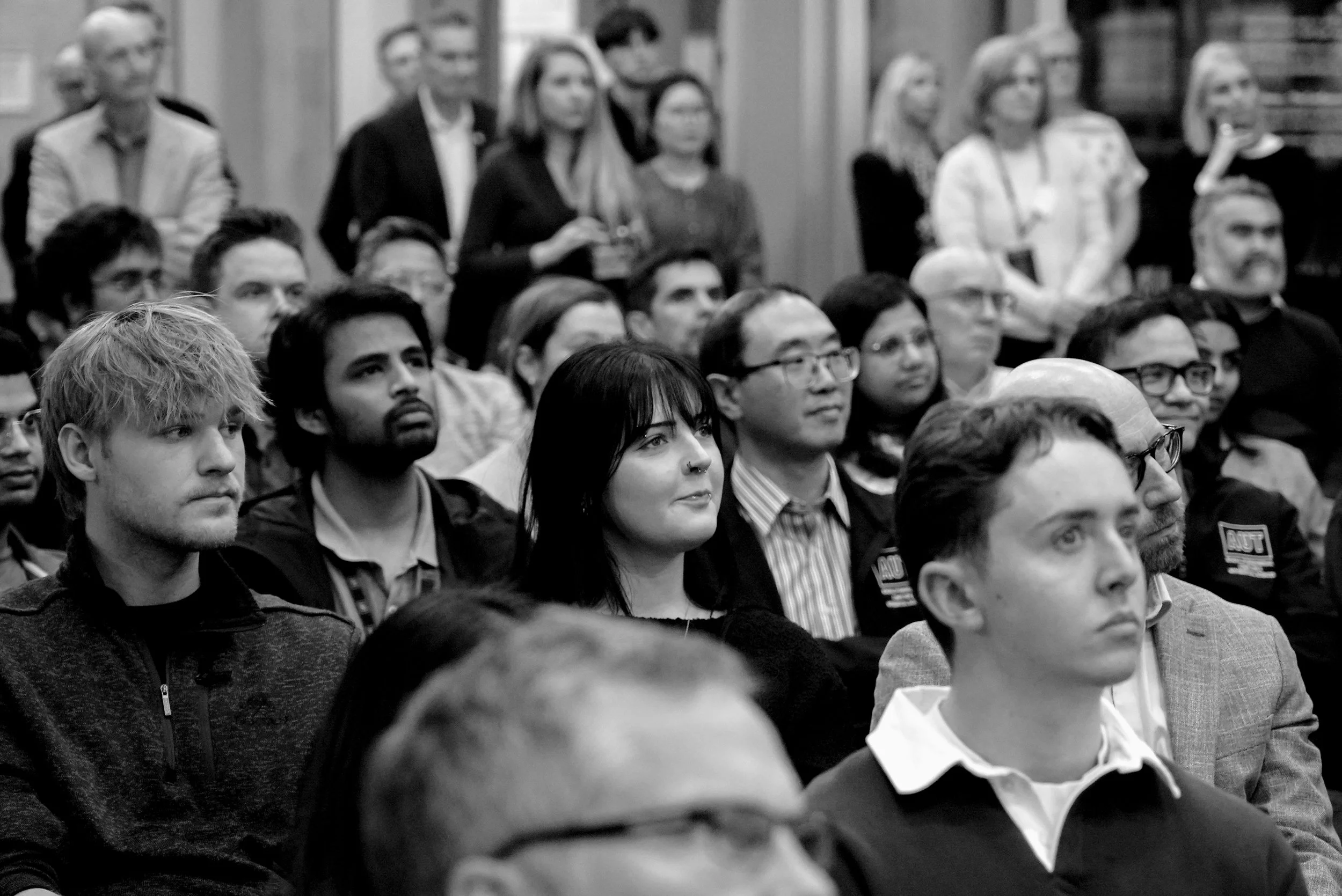 Audience seated and listening attentively at a conference or seminar, with a diverse group of men and women in the audience.