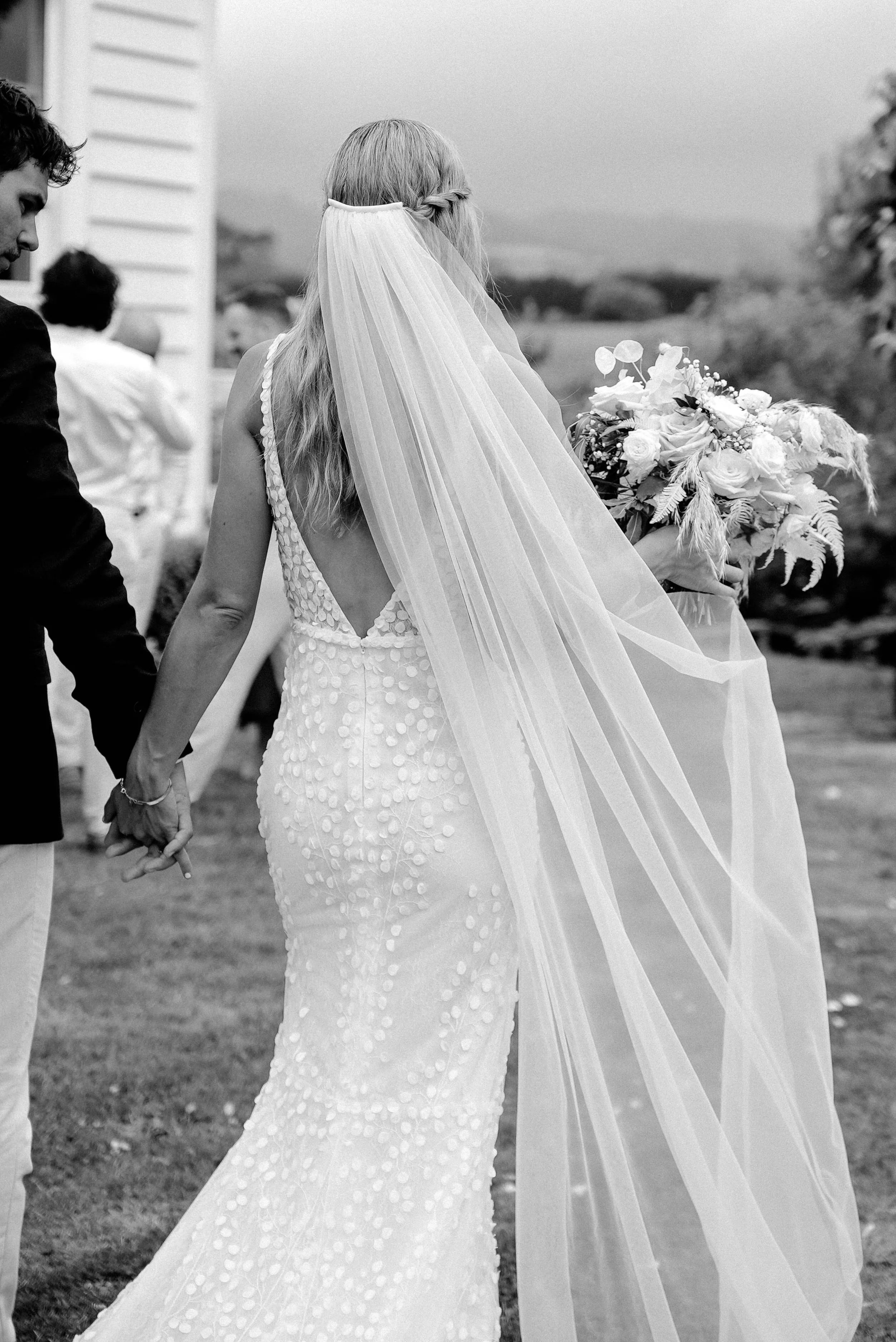 A bride in a wedding dress holding a bouquet, walking with a man and holding hands, during an outdoor wedding ceremony.