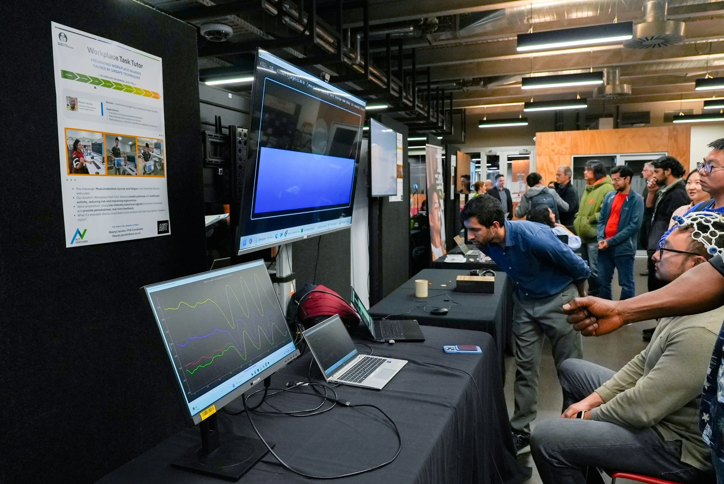 Group of people observing a science or technology exhibition with computers and monitors displaying data and graphs.
