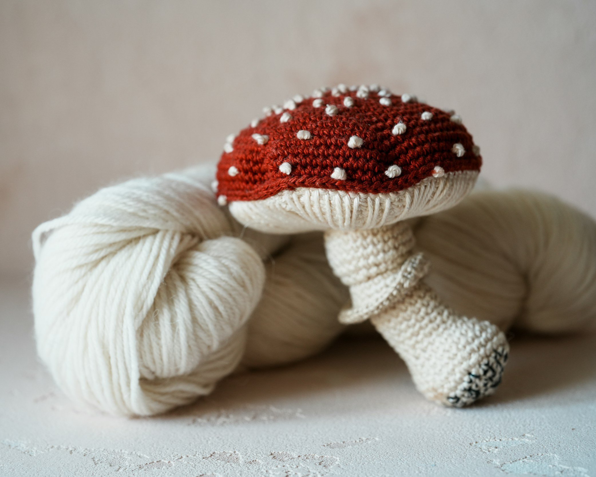 Champignon crocheté rouge et blanc avec un écheveau de laine blanche.