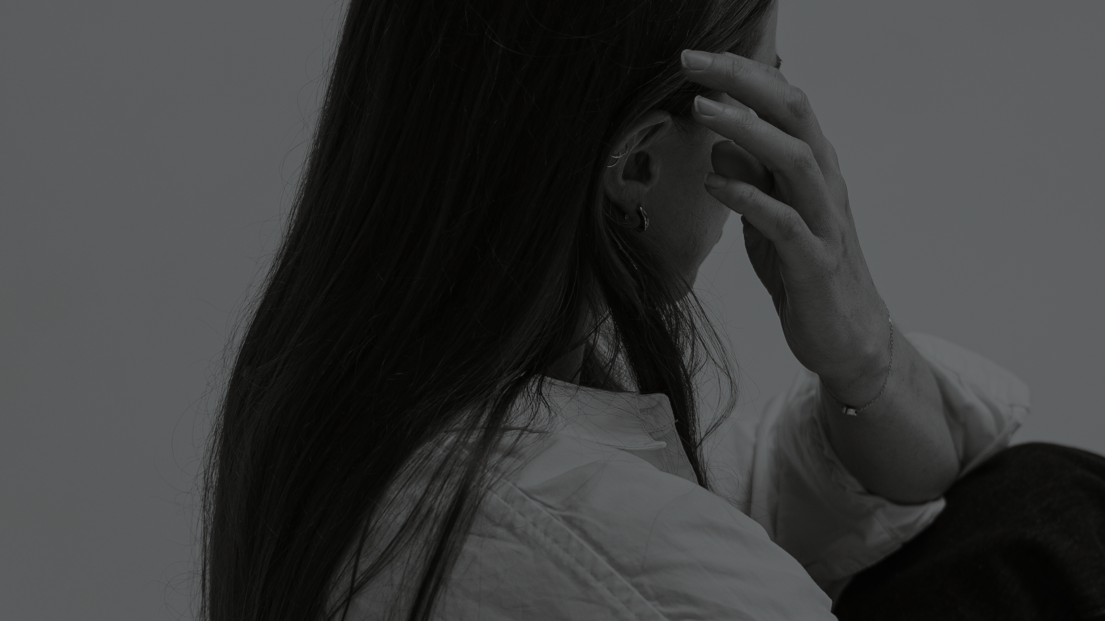 A person with long hair is resting their head in their hand, with their face turned away and partially covered.