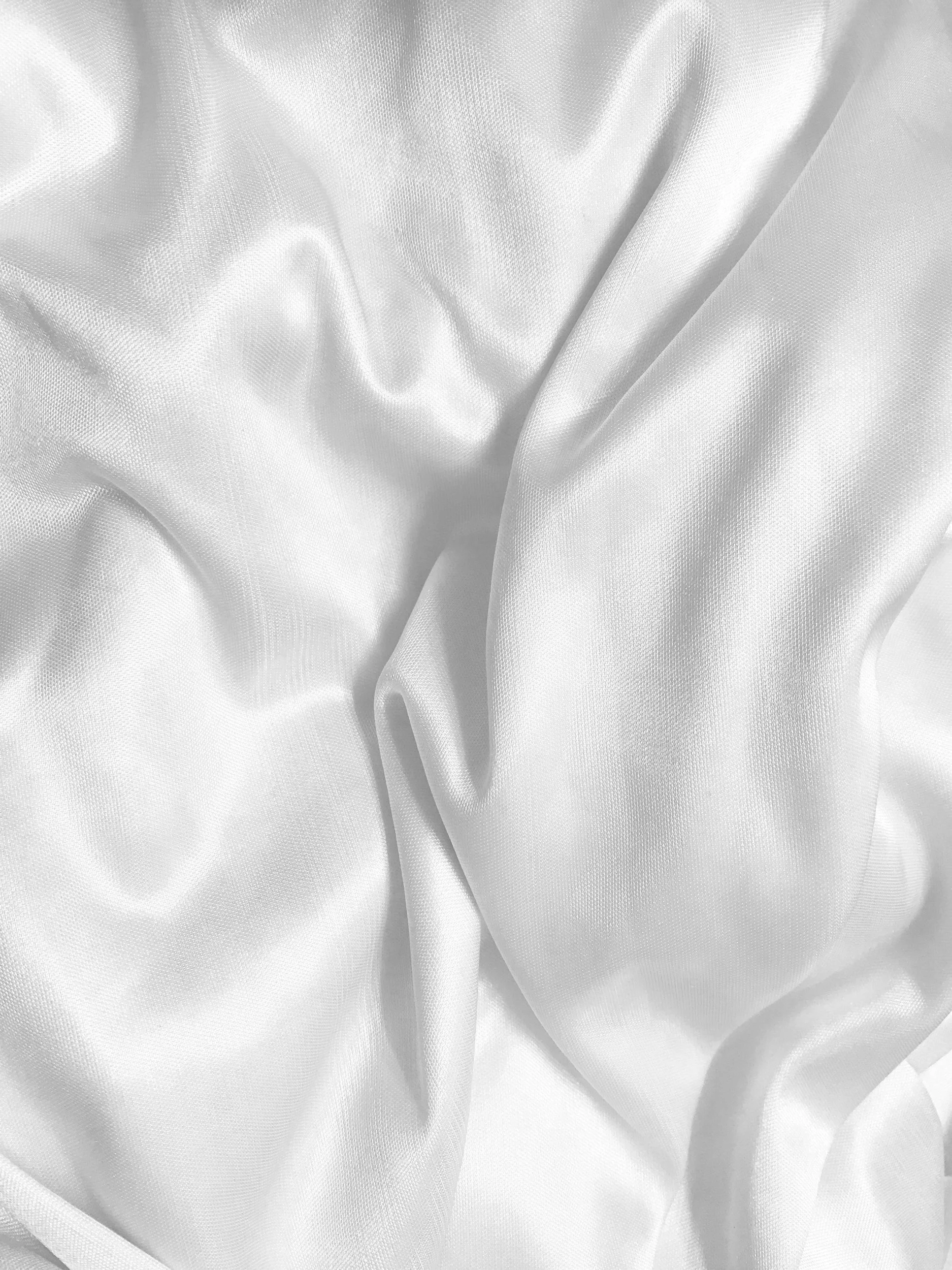 Close-up of white satin fabric with wrinkles and folds.