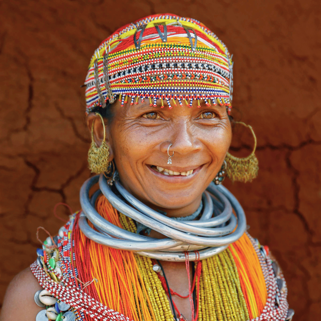 Smiling person wearing colorful traditional beadwork and jewelry with a beaded cap.