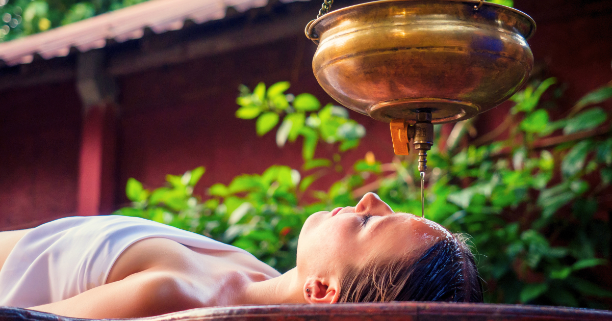 Shirodhara Ayurvedic treatment with warm oil being poured from a brass vessel at a Kerala retreat