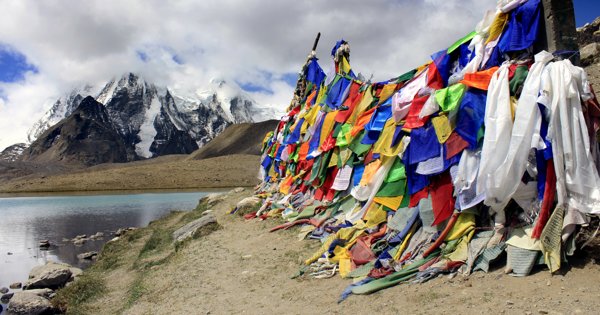 Buddhist prayer flags beside Gurudongmar Lake in North Sikkim with a snow-covered Himalayan peak in the background