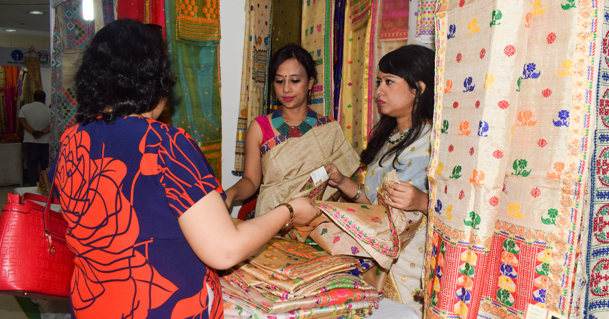 women examining Muga silk at textile fair, Assam