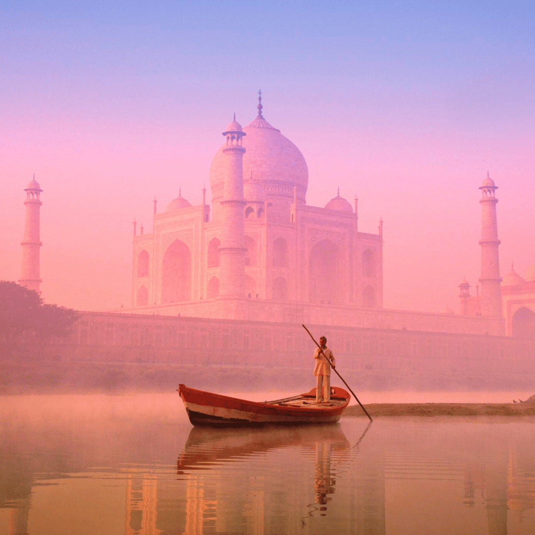 The Taj Mahal at sunrise or sunset with a person in a boat on the river in front of it.