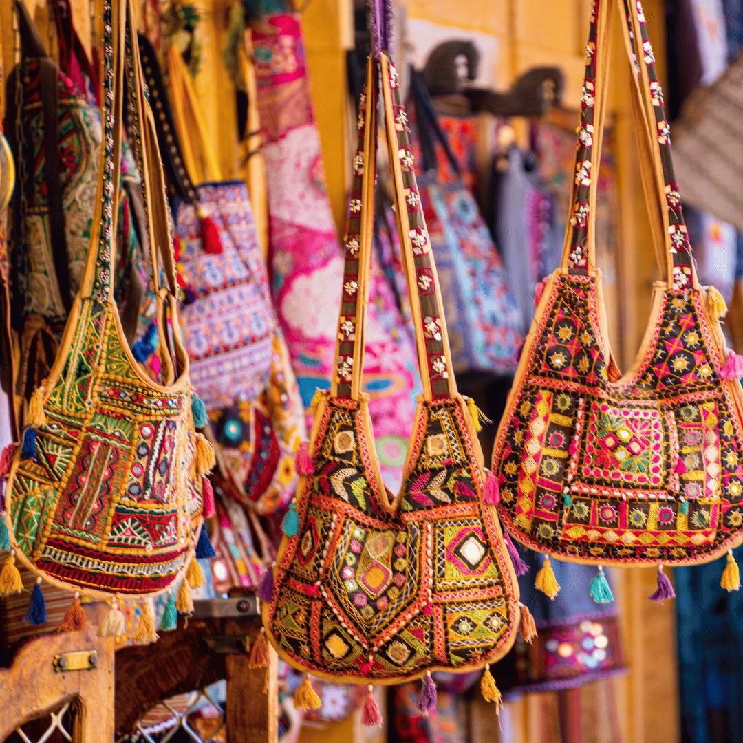 Colorful embroidered handbags hanging at a market stall, with intricate patterns and tassels.