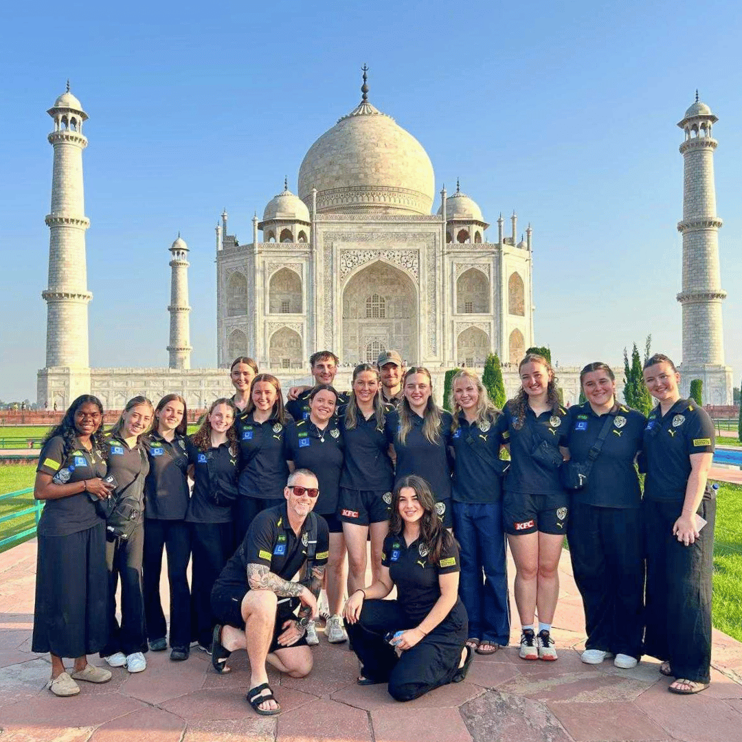 Group of people wearing matching black outfits posing in front of the Taj Mahal.