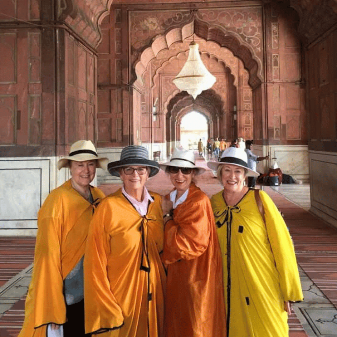 Four people wearing hats and yellow robes standing inside a historic archway with a chandelier above them.