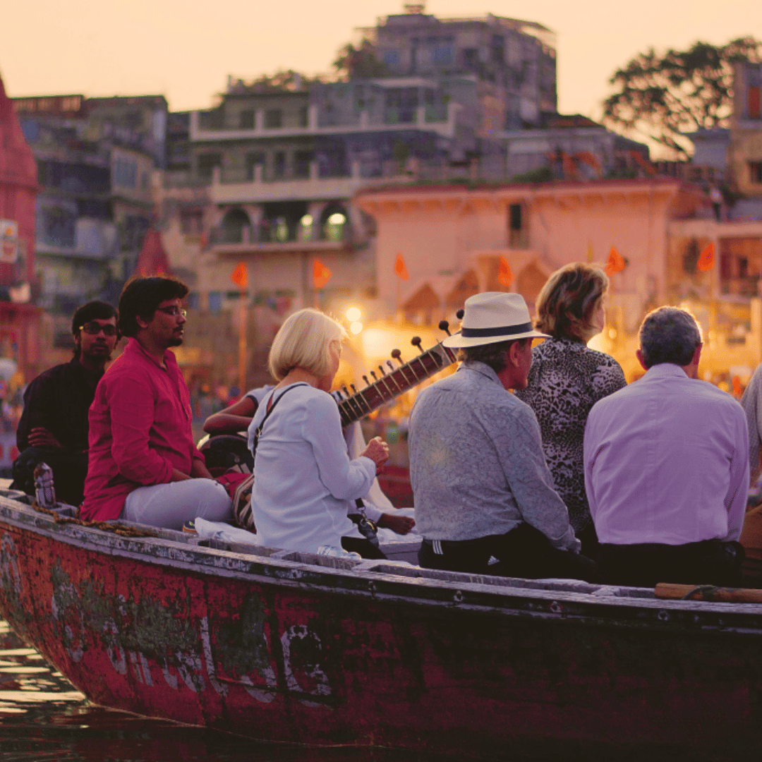 Group of people in a boat on a river near a brightly lit structure at sunset.
