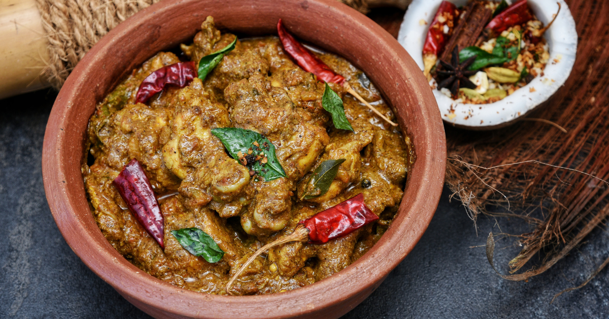 Spiced chicken curry and white rice on a banana leaf, with dried chillies and whole spices beside them.