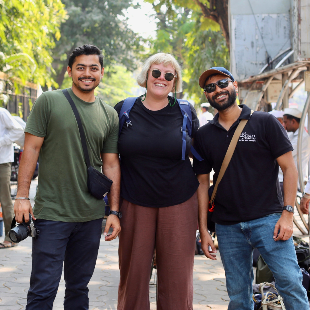 Three people smiling outdoors, with trees and a busy street in the background.