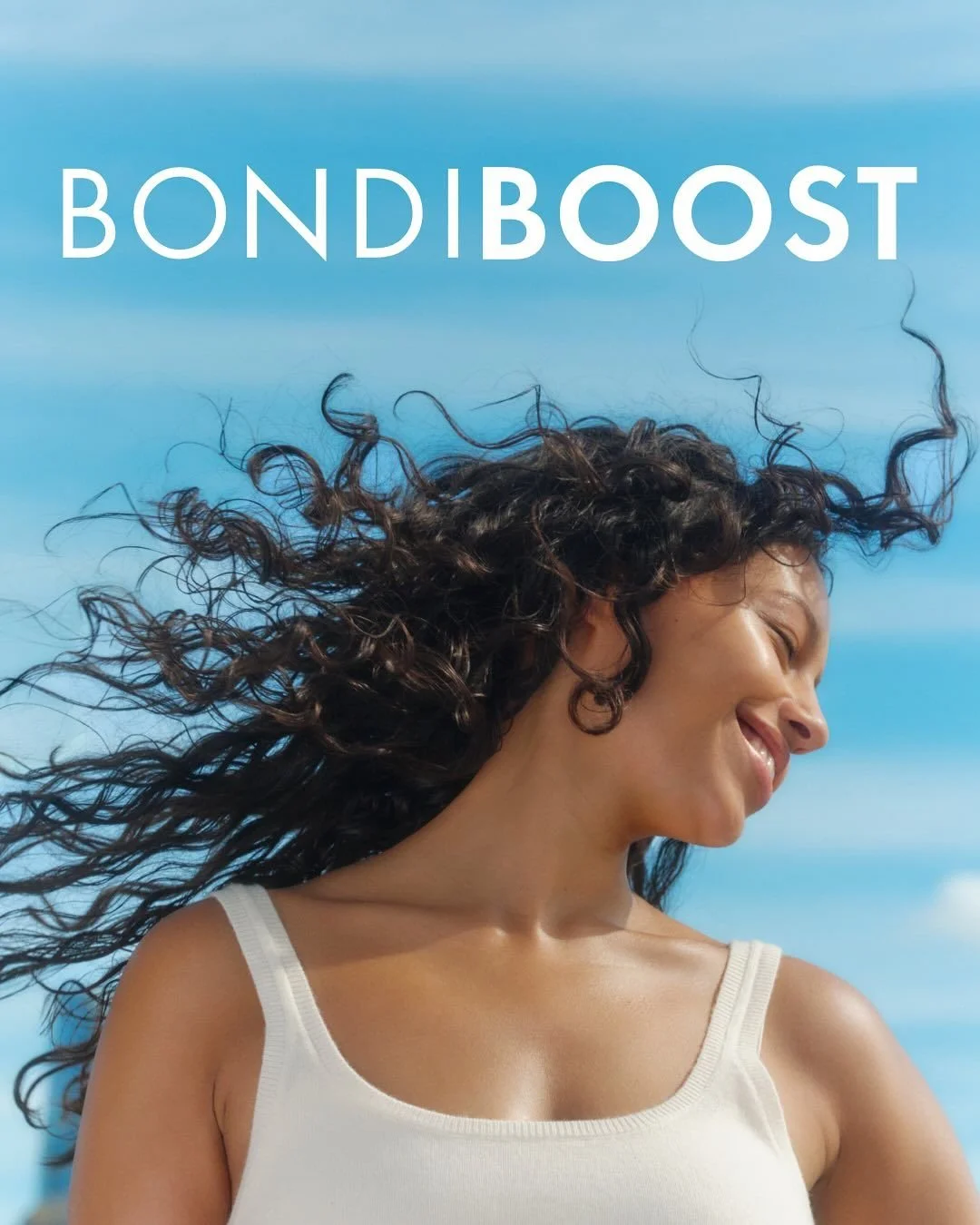 Woman smiling outdoors with hair blowing in the wind, blue sky in the background, and the text 'BONDIBOOST' at the top.