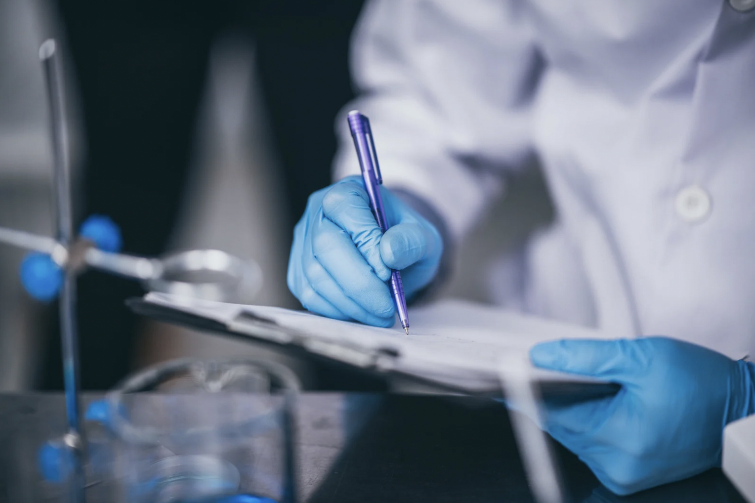 Un scientifique portant des gants bleus écrit sur un clipboard dans un laboratoire.