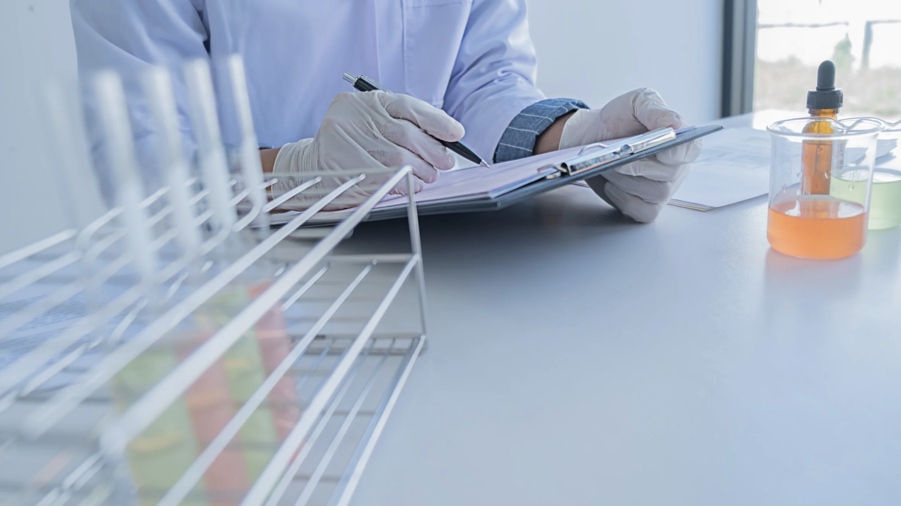 Un scientifique en laboratoire écrit dans un carnet à la main, entouré de tubes à essai et de flacons contenant des liquides colorés.