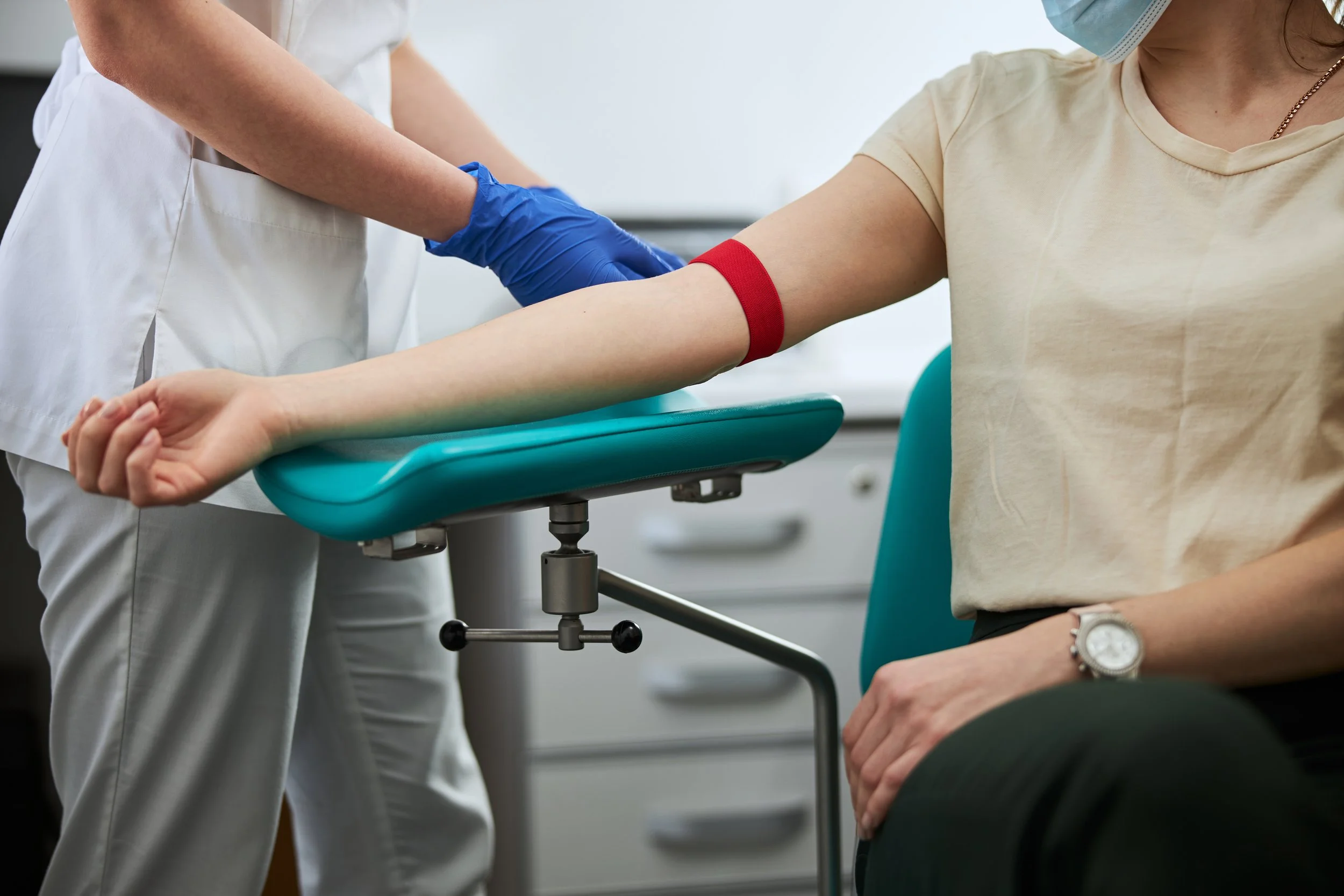 Une femme donne son sang dans une clinique à Deux-Montagnes, une infirmière aide et porte des gants bleus pour le prélèvement sanguin.