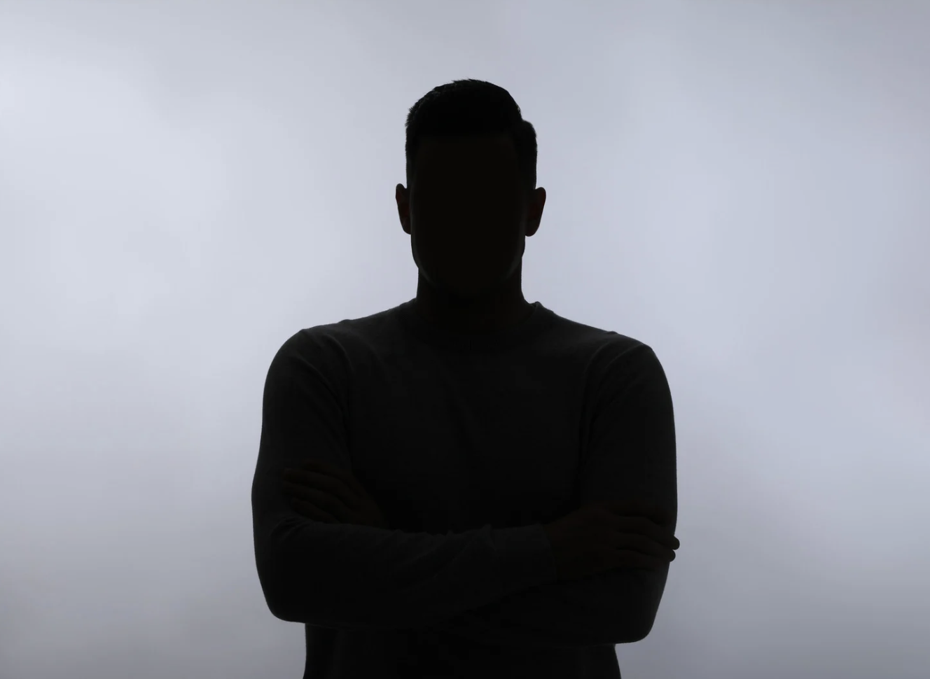 Silhouette d'une personne avec bras croisés, de face, contre un ciel gris.