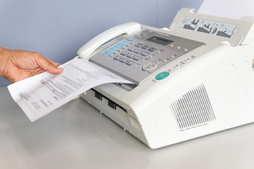 Une photocopieuse en train de photocopier un document. Une main tenant une feuille de papier sortant de la machine.