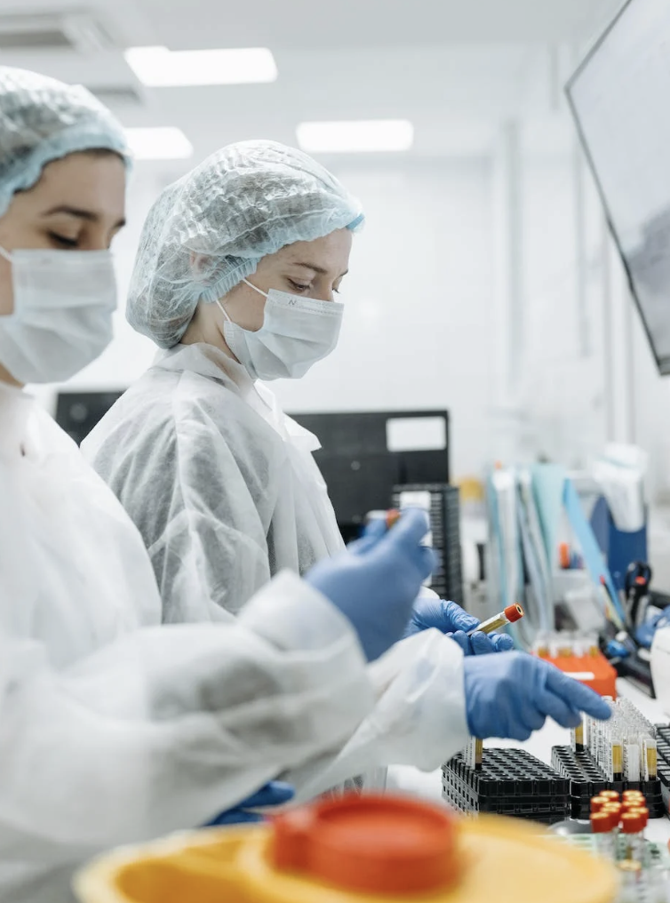 Trois scientifiques portant des vêtements de protection, des masques, et des gants dans un laboratoire, manipulant des échantillons sur une surface de travail.