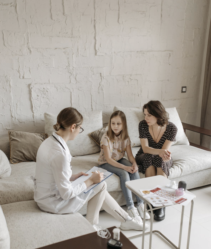 Une consultation médicale où une doctoresse discute avec une jeune fille et une adulte dans un salon