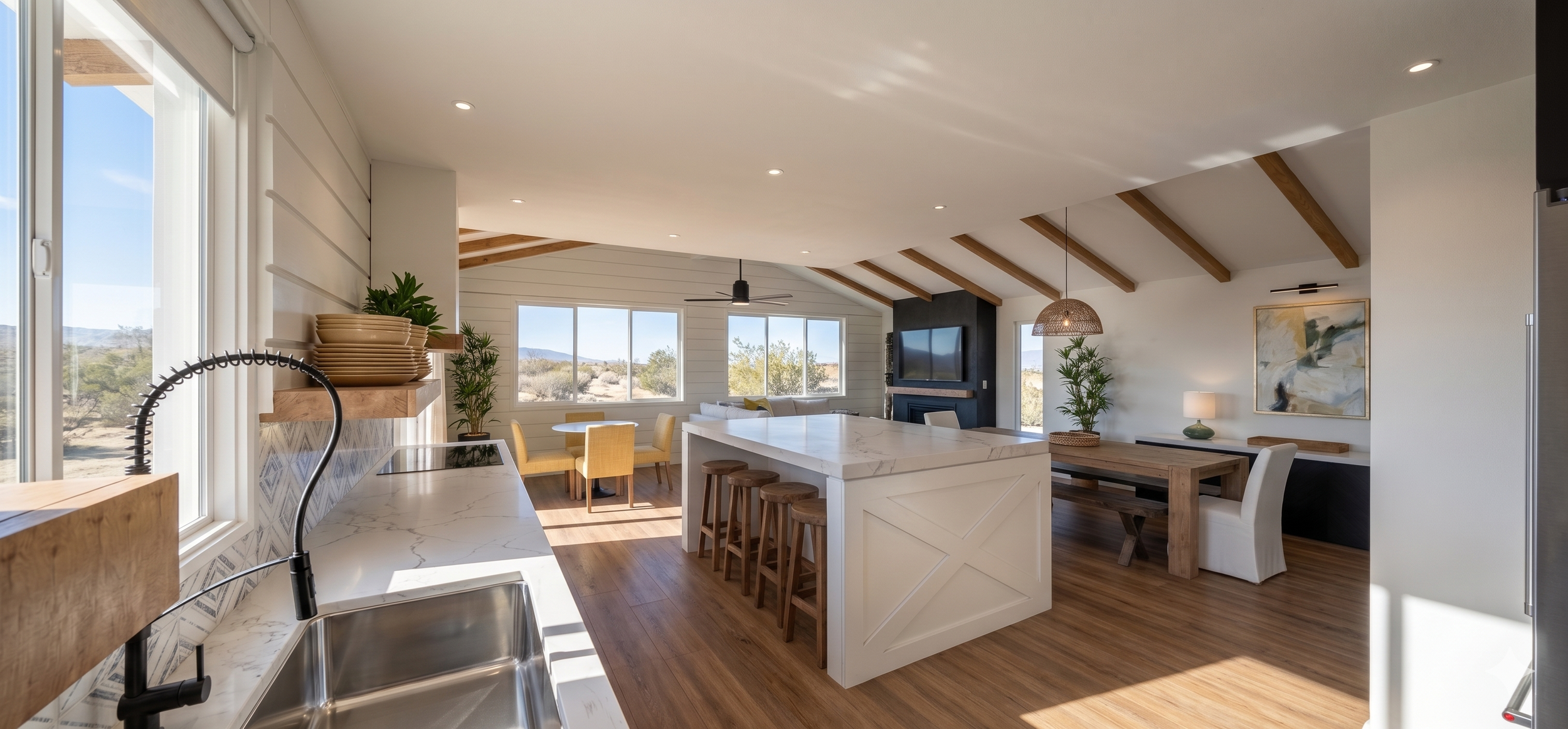 Open-concept living and dining area with large windows showing desert landscape, featuring wooden beams, a fireplace, and modern furniture.