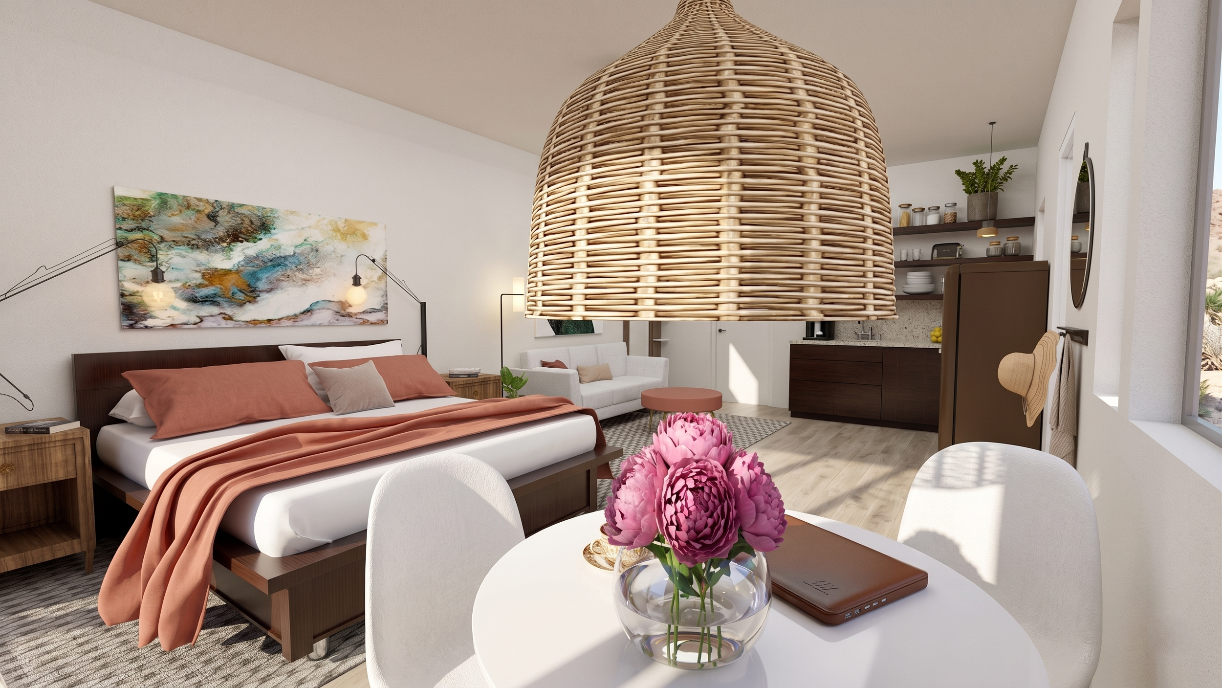 A modern living space with a bed, a white sofa, and an open kitchen, featuring a large woven pendant light, colorful artwork on the wall, and a table with a glass vase of pink flowers.