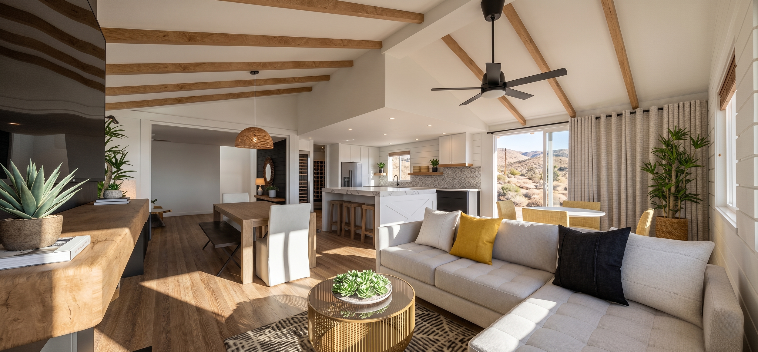 Bright living room with wood beams on ceiling, ceiling fan, large windows showing desert landscape, beige sofa with yellow and black pillows, wooden coffee table with plants, dining table with chairs, modern kitchen in background.