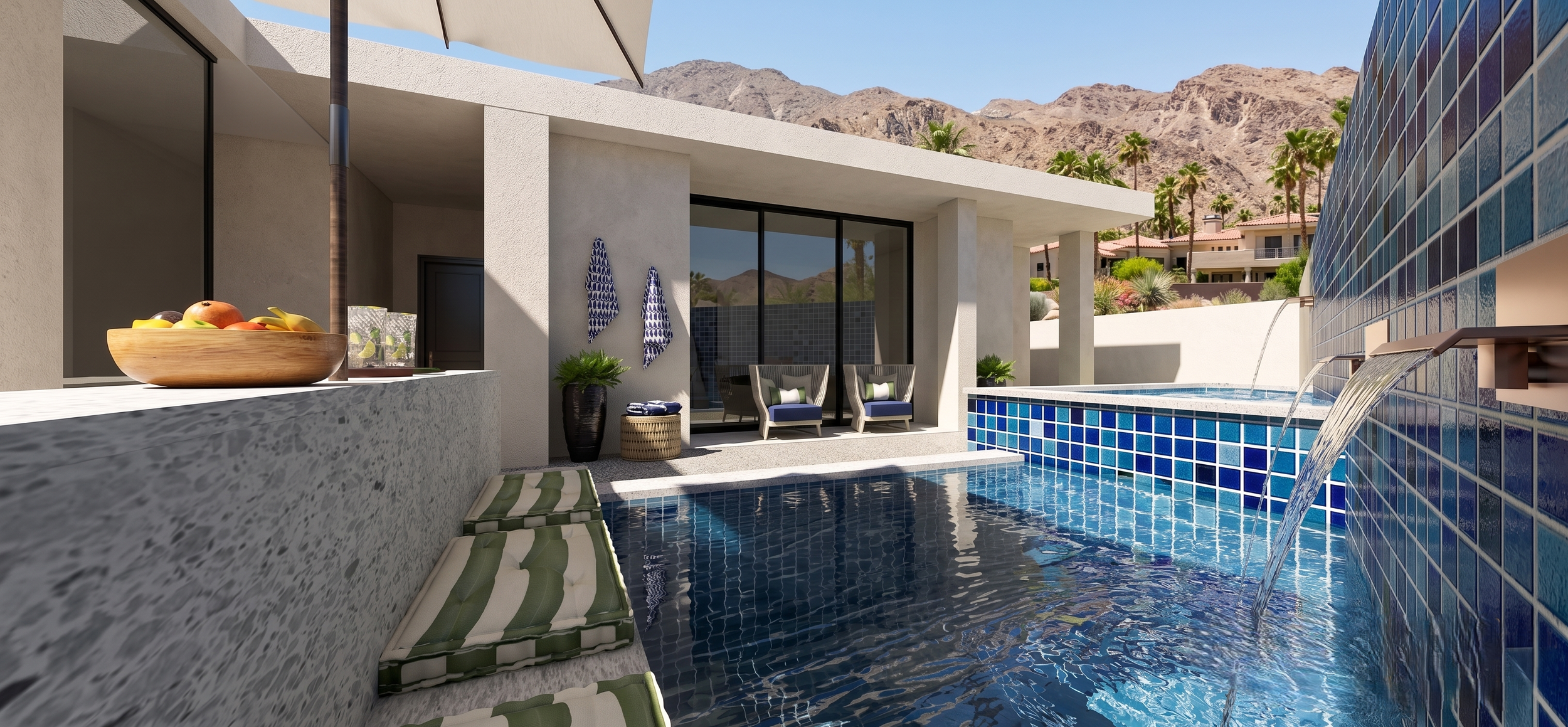 A modern backyard pool area with blue tiled pool, water feature, and seating area with chairs and cushions, surrounded by desert landscape and mountains in the background.