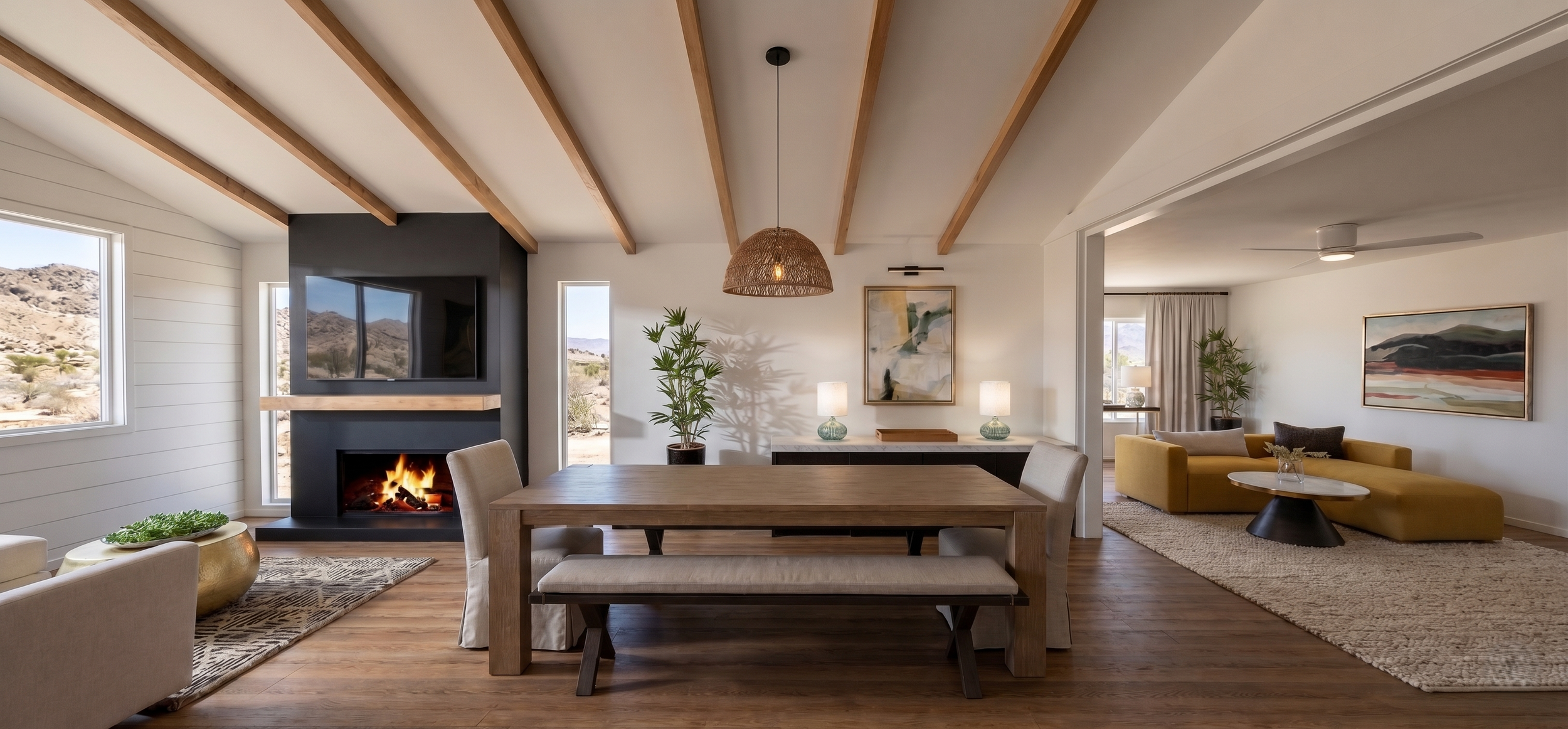 Living room with a dining table, beige chairs, yellow sofa, modern fireplace, wall-mounted television, artwork, lamps, and desert landscape outside windows.