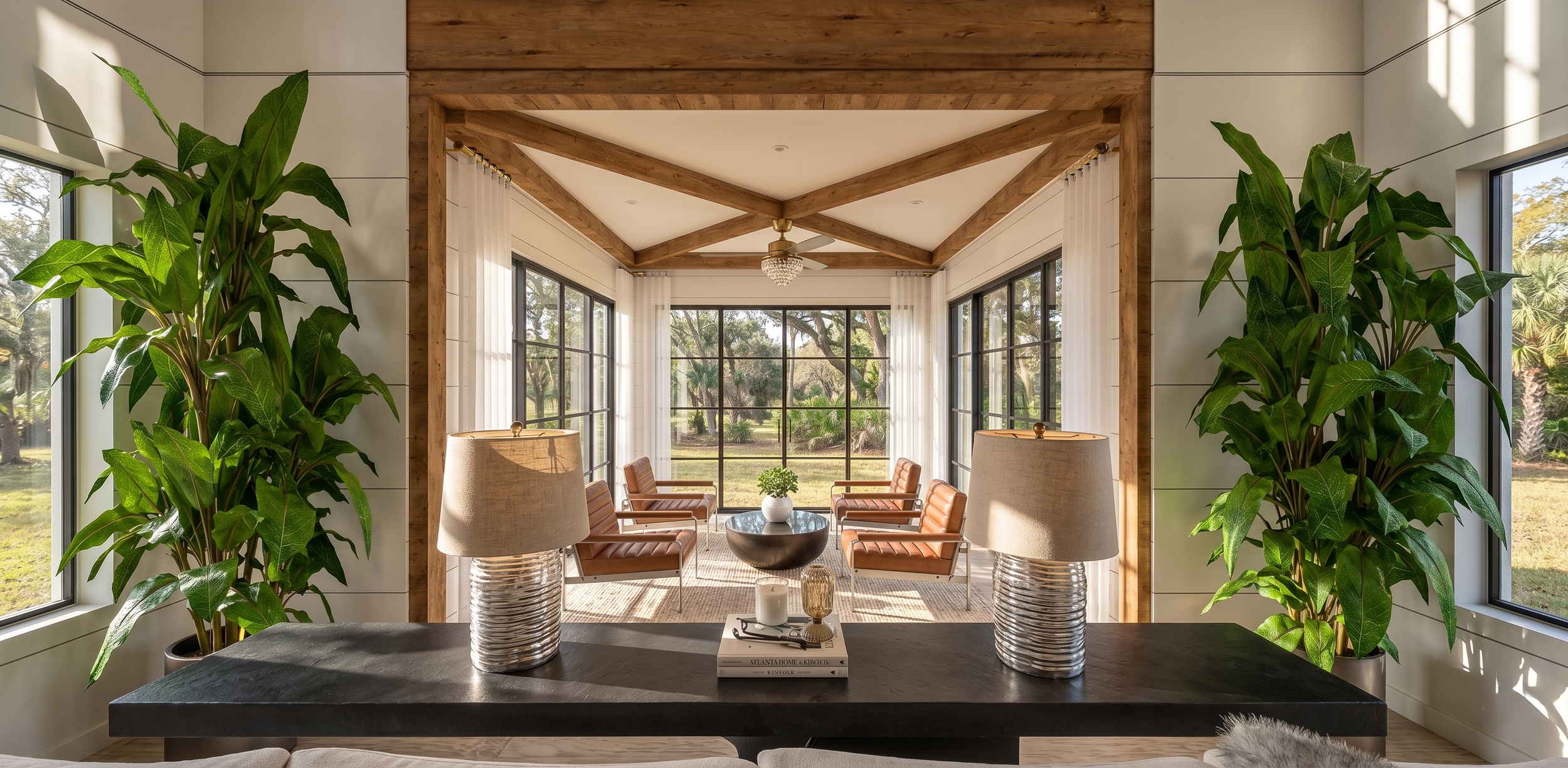 Living room with large windows, wooden beams, and a view of an outdoor garden. There are six chairs, two lamps, a coffee table with a plant, and a chandelier overhead.