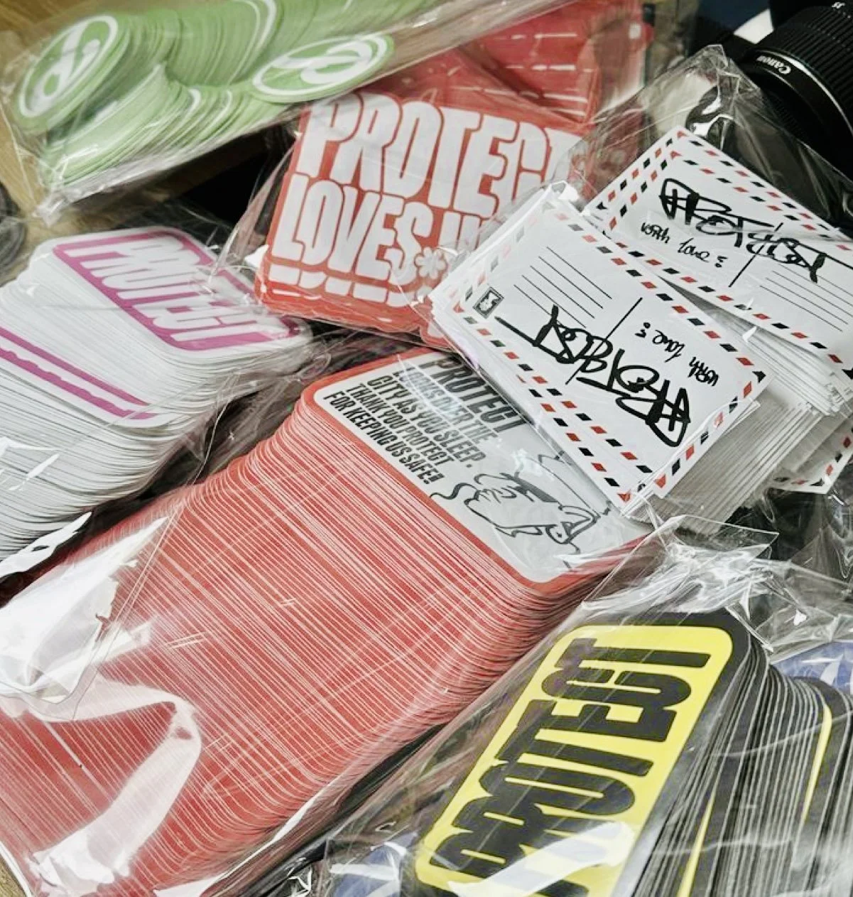 Assorted safety and greeting labels for mail and packages, including 'Protect Loves', 'Handle with Care', and 'US POST' stickers, in clear plastic packaging.