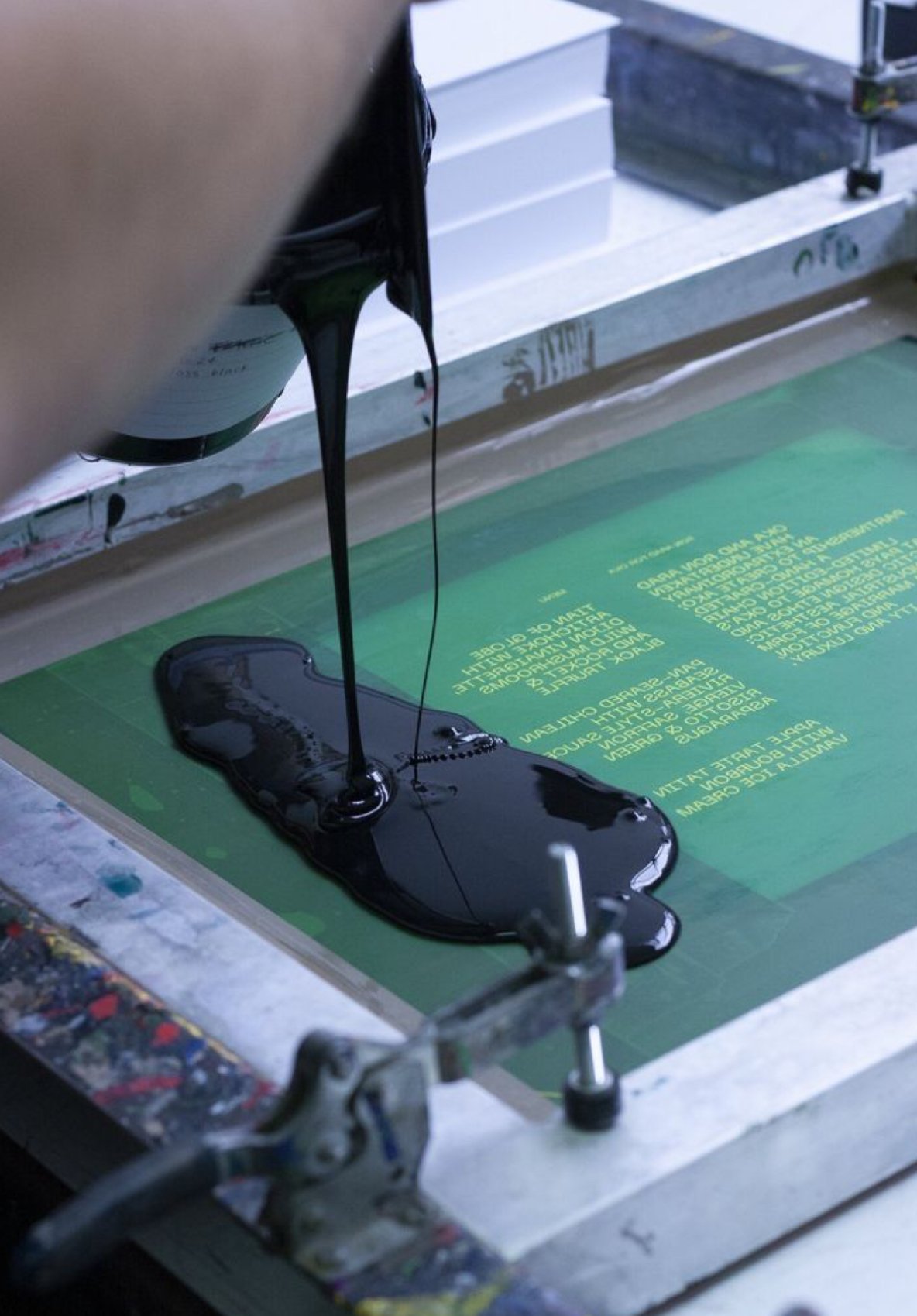 Close-up of black ink pouring onto a printing screen during printmaking process.