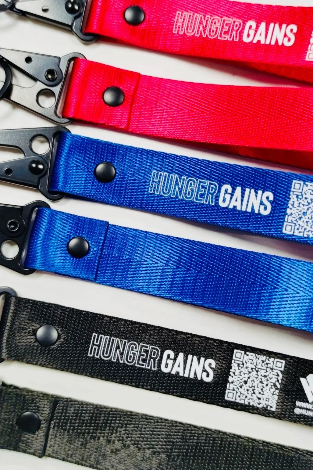 A collection of fitness straps in red, blue, black, and gray colors, with the phrase 'HUNGER GAINS' printed on each, arranged on a white surface.