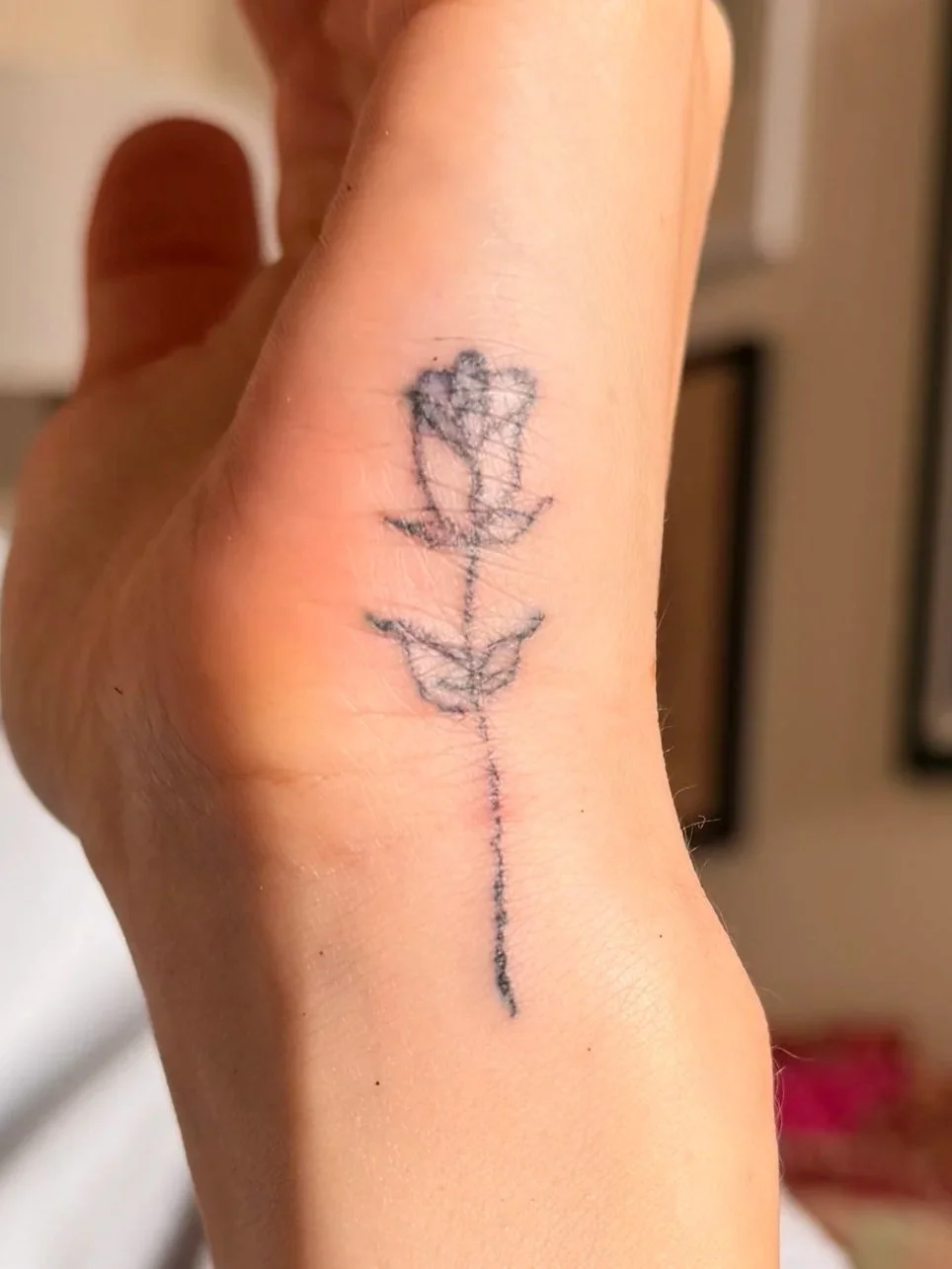 A close-up of a person's hand showing a tattoo of a simple outline of a rose on the finger.