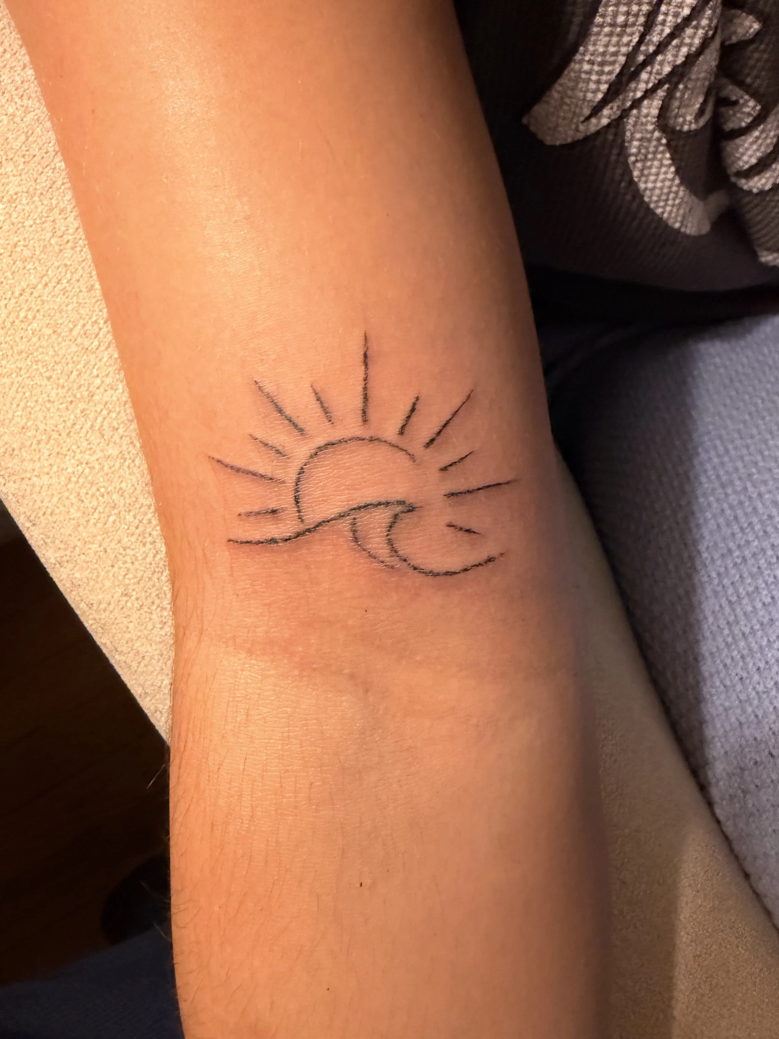 Tattoo of a sunset and a wave on a person's forearm.