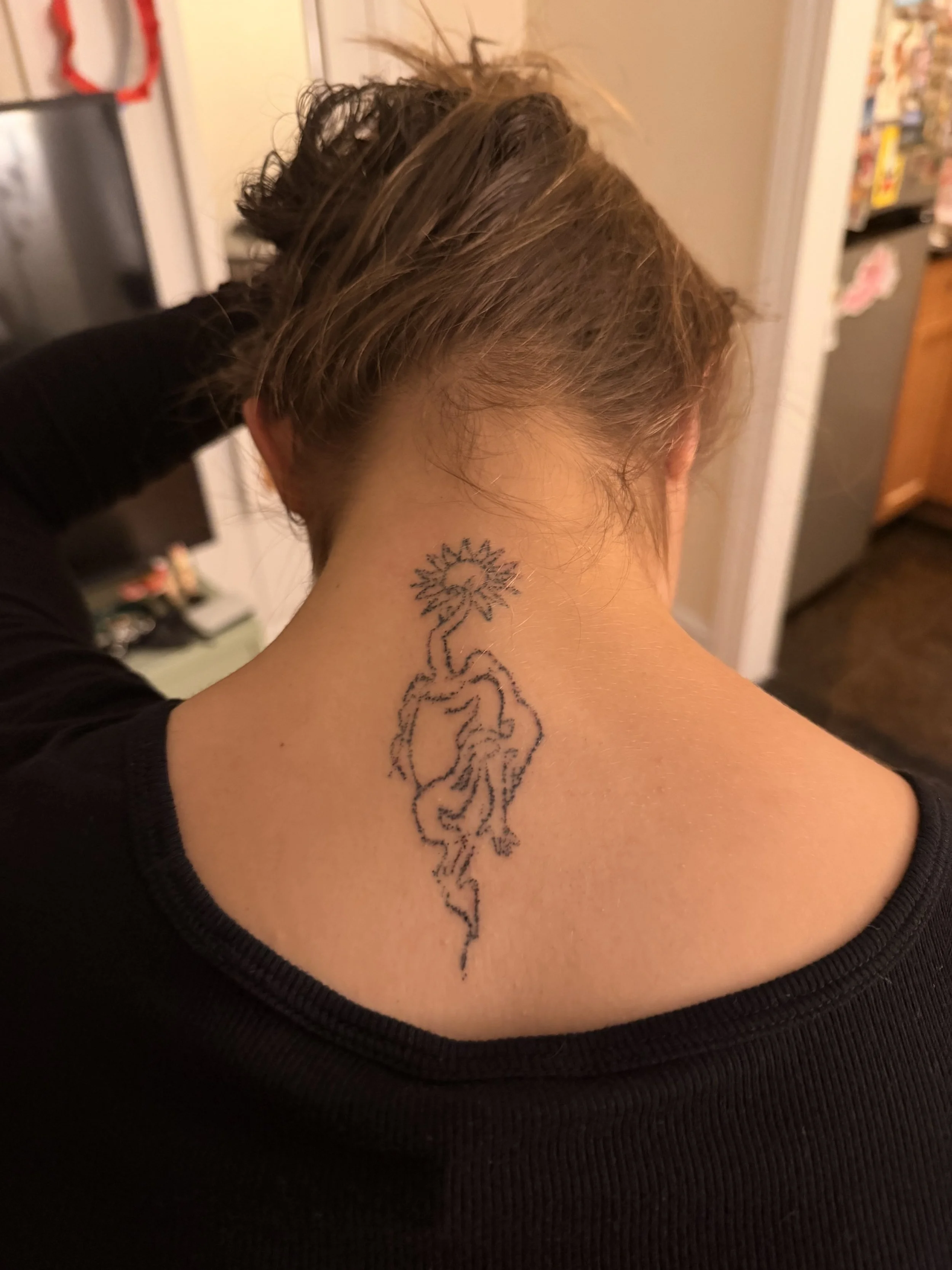 Back of a person's neck with a tattoo of a lion and a tree in black ink.