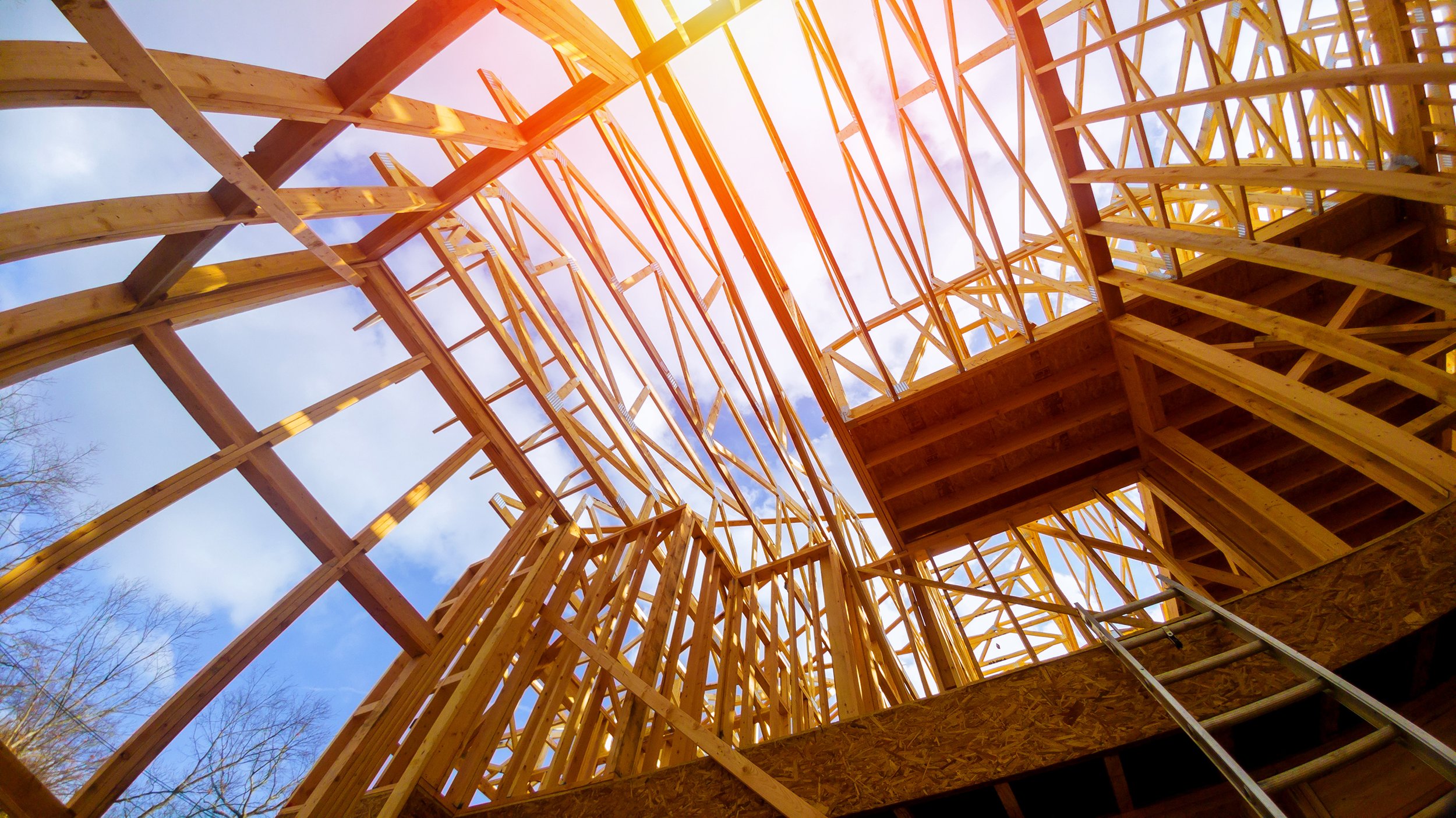 Wooden house frame under construction with blue sky and sunlight.