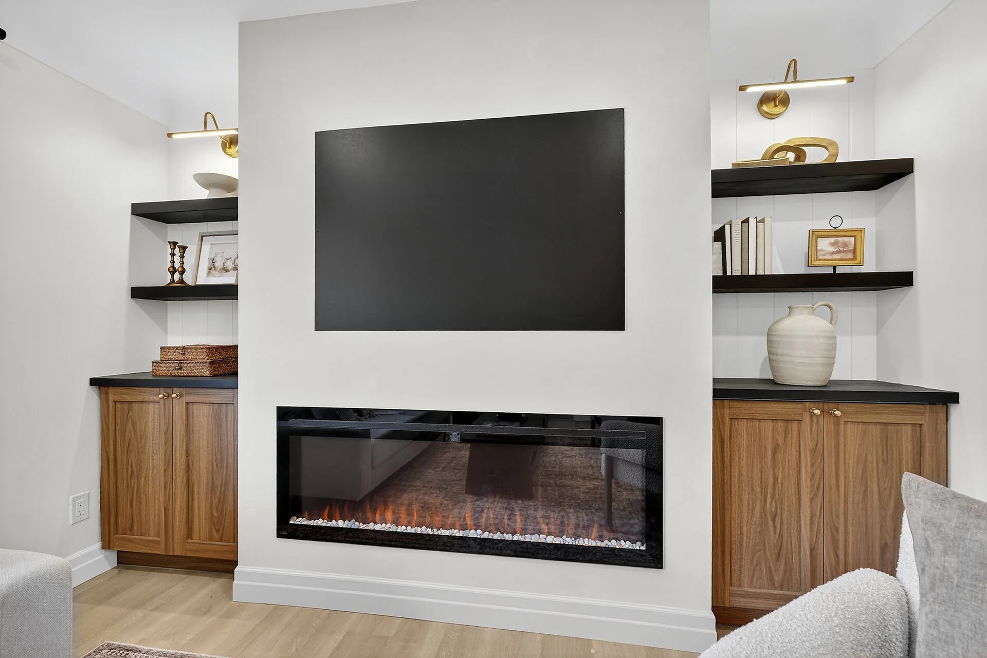 Living room with built-in wooden cabinets and black shelves surrounding a modern fireplace with orange flames. A large blank blackboard is mounted on the wall above the fireplace, with books, framed pictures, and decorative objects on the shelves.