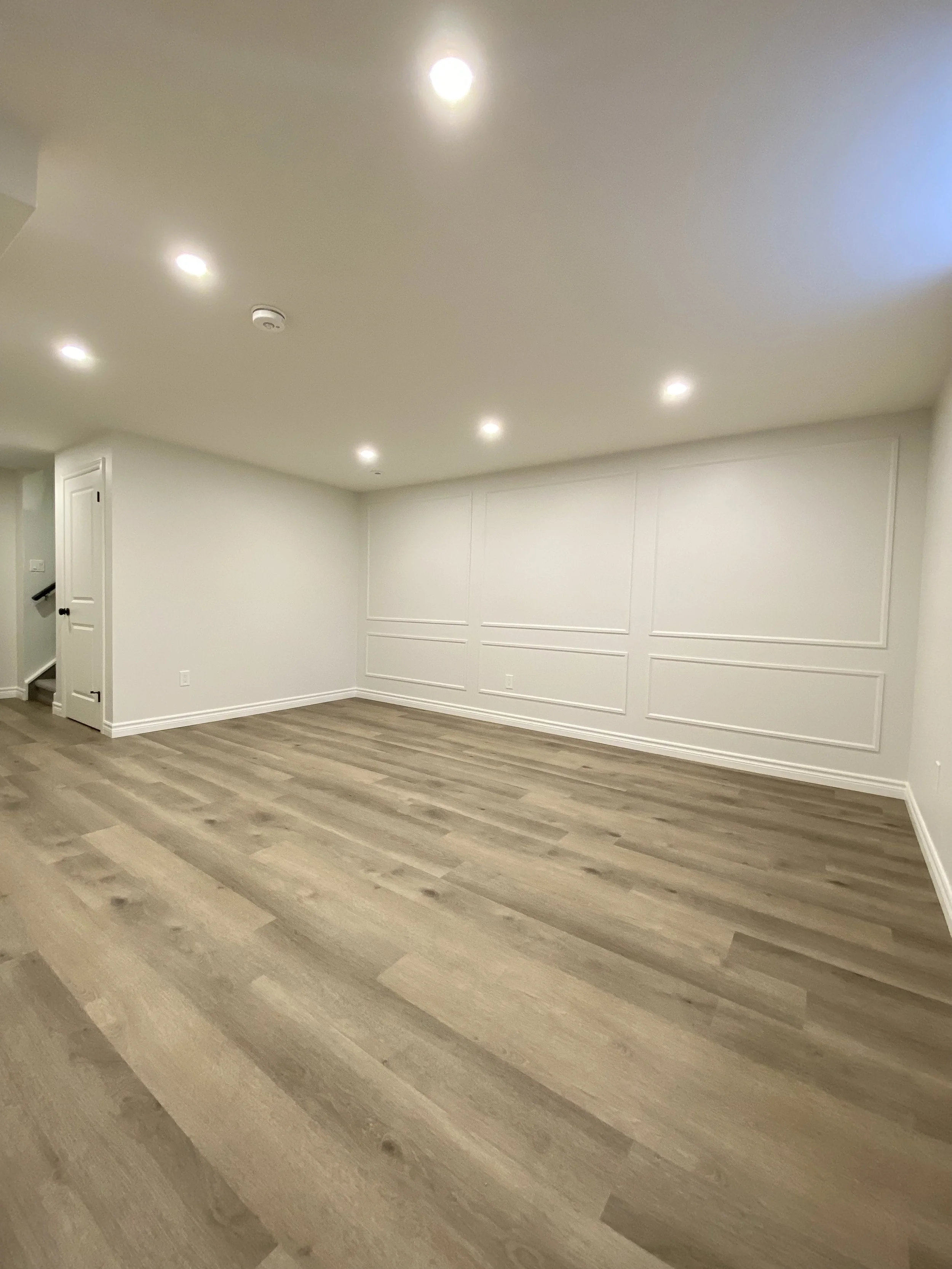 Empty room with white walls, wooden flooring, and ceiling lights.
