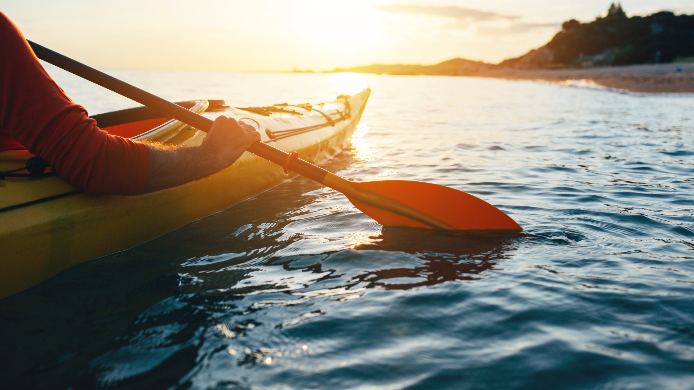 Person in kayak with paddle in ocean in front of sunset on the water
