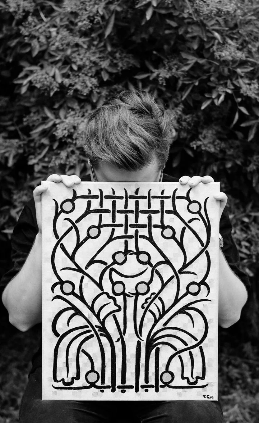 Person with short hair holding the "Generations" painting on a canvas, obscuring their face, outdoors with foliage in the background.