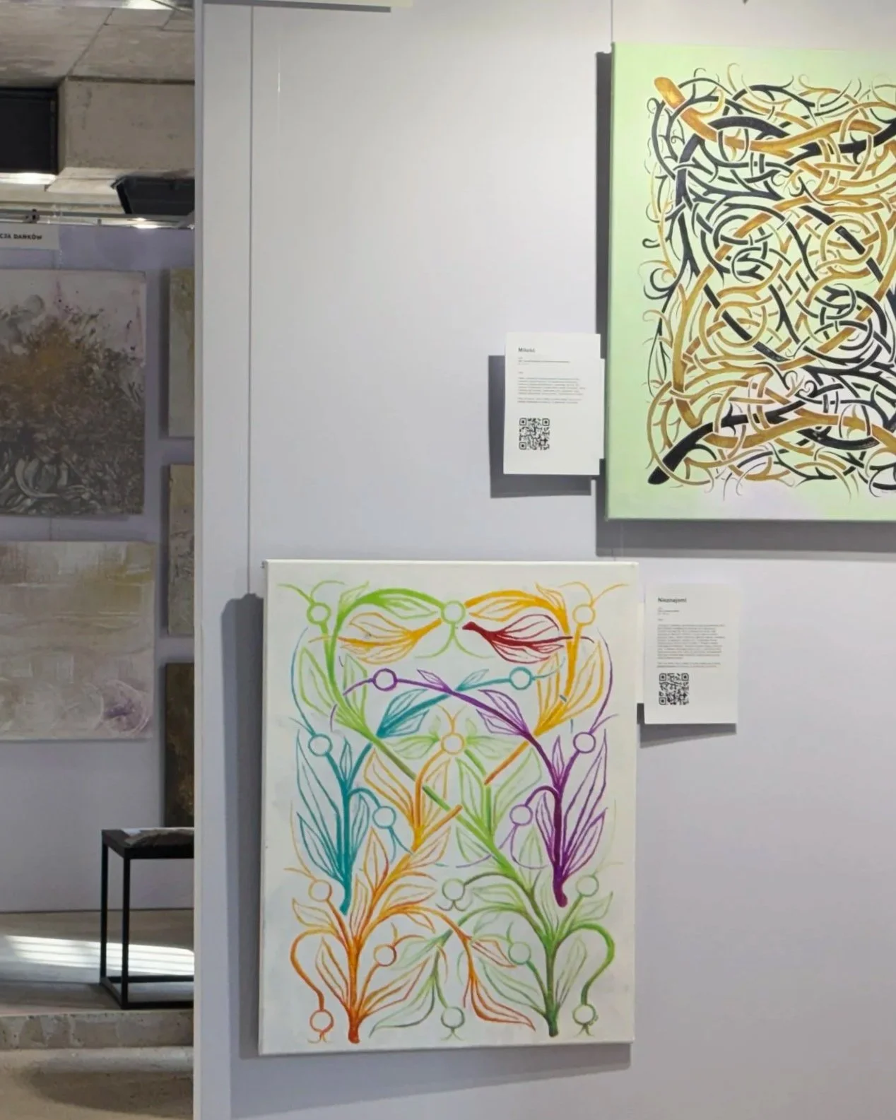 Colorful abstract paintings depicting interconnected floral patterns in rainbow hues on a white canvas, displayed in an art gallery.
