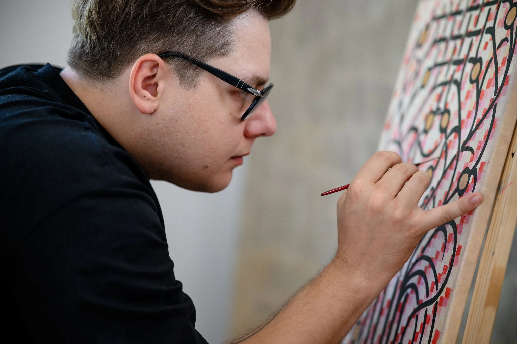 Peter Gil is painting on a colorful, patterned canvas, focusing on their artwork.