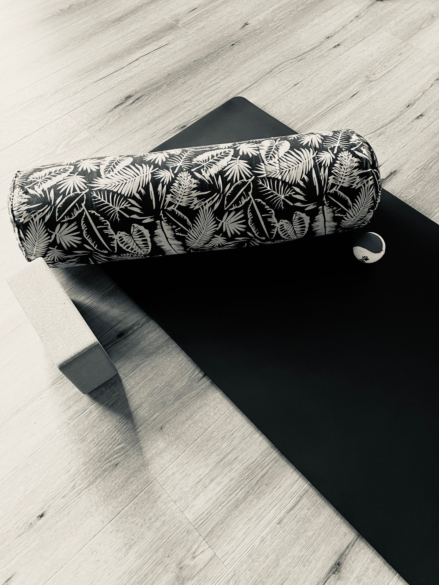 Yoga mat and bolster cushion on a black yoga mat, placed on a light-colored wooden floor.