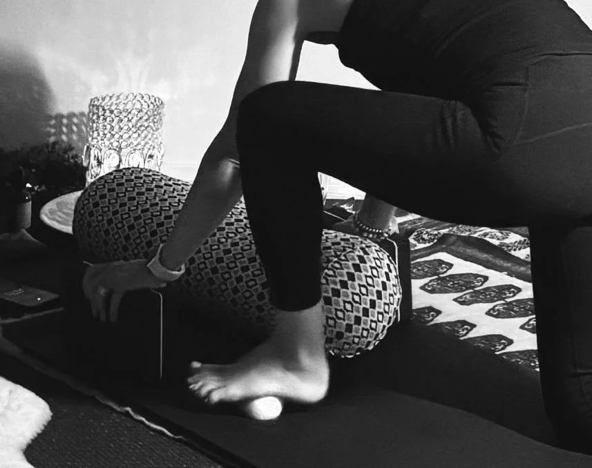 Person performing a foot massage or stretching on a person lying down on a mat, in a room with decorative pillows and a side table with a lamp.