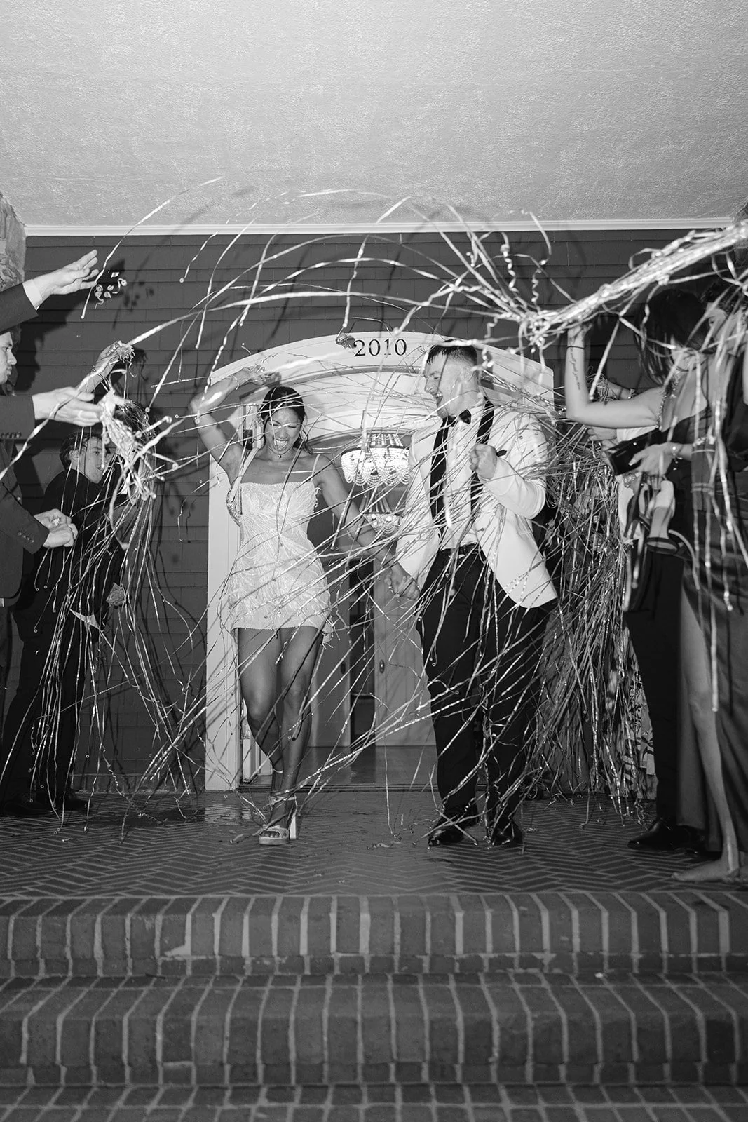 People celebrating at a wedding reception with streamers and confetti, with a bride and groom walking through the entrance labeled 2010.