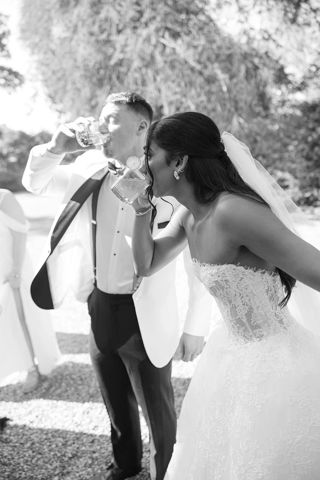 A bride and groom drinking from large glasses at an outdoor wedding reception.