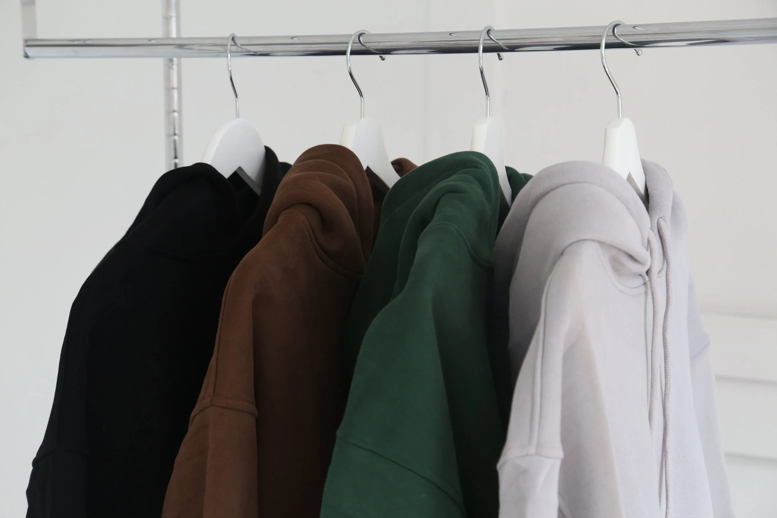 A row of hoodies in black, brown, green, and white hanging on a metal rack.